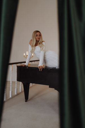 Elegant woman in white dress leaning on black piano. Loft interior.の写真素材
