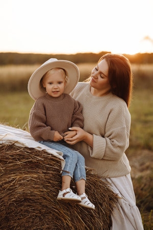 Front view of a young mother and her daughter sitting by a haystack, smiling at each other.の写真素材