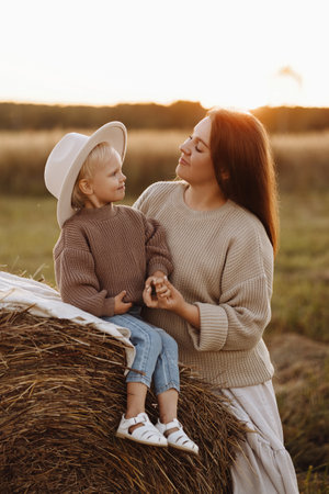 Front view of a young mother and her daughter sitting by a haystack, smiling at each other.の写真素材