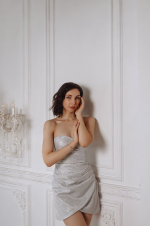 Young woman in silver dress posing against white classic wall in elegant roomの写真素材