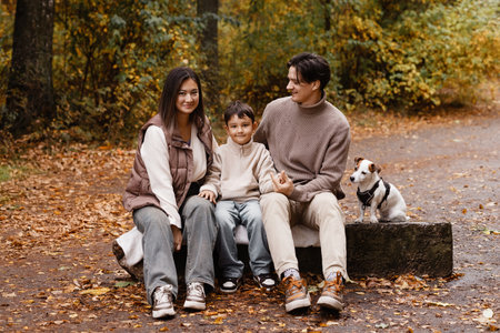 Happy family of three with dog sitting on bench in autumn park