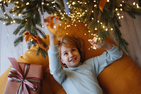 Smiling child top view under Christmas tree with gift box on orange cushion on wooden floorの写真素材