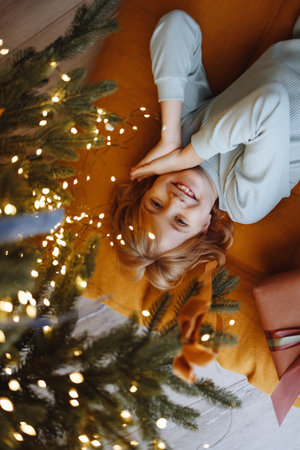 Smiling child top view under Christmas tree with gift box on orange cushion on wooden floorの写真素材