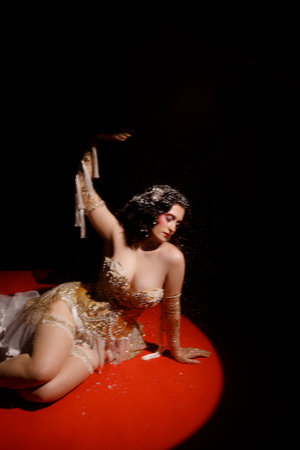 Woman in vintage corset lying on red stage floor under hanging beads on dark background