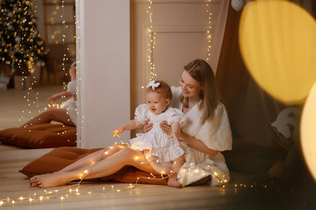 Mother playing with baby girl on floor in cozy kids room with wooden horse and soft pillowsの写真素材