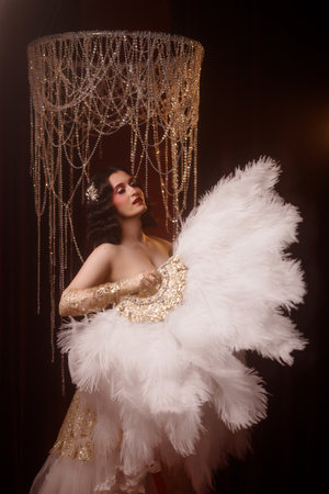 Young woman in vintage corset costume posing under chandelier on dark background