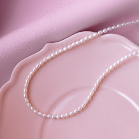 Pearl necklace on pink ceramic plate and wooden table in natural lightの写真素材