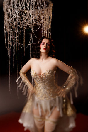 Circus show performer in vintage corset costume under chandelier on dark background