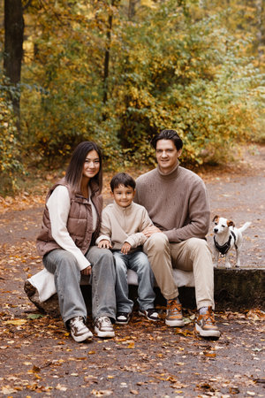 Happy family of three with dog sitting on bench in autumn parkの写真素材