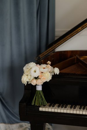White rose bridal bouquet and two gold wedding rings placed on a black piano.の写真素材