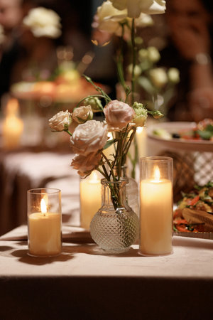 White roses in glass vases with burning candle on table with dark backgroundの写真素材