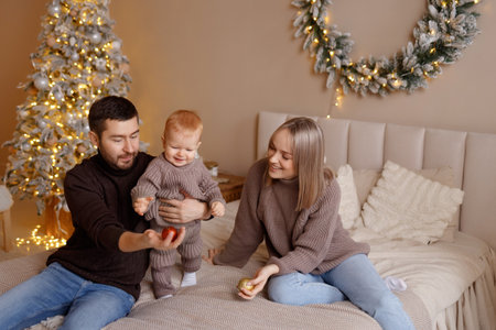 Young family with toddler playing on bed in cozy bedroom with beige wall and wreathの写真素材
