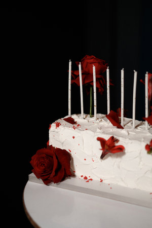 Wedding cake with red roses and lit candles on wooden table with dark backgroundの写真素材