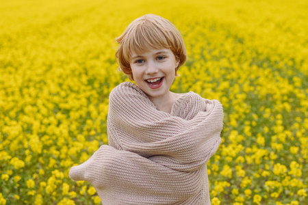 Smiling girl in oversized beige sweater hugging herself in yellow flower fieldの写真素材