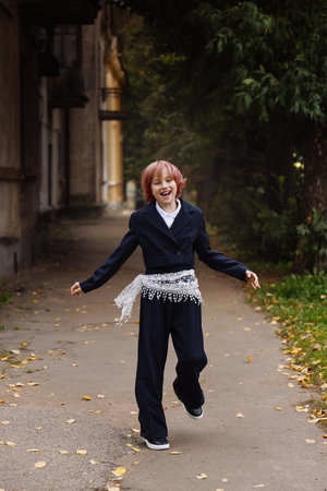 Happy schoolgirl with pink hair in navy uniform running outdoors near old building, front viewの写真素材