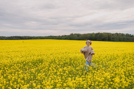 Smiling 9 year old girl in oversize sweater running in yellow rapeseed field