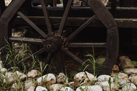 Old wooden wagon wheel on rustic background with stones and green grassの写真素材