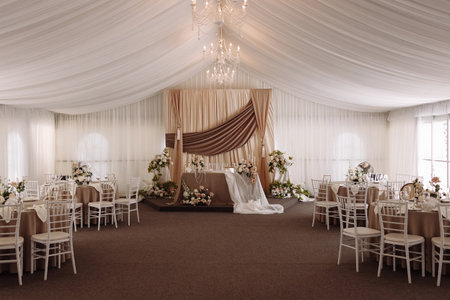 Wedding banquet hall with elegant stage and round tables decorated in beige and white tonesの写真素材
