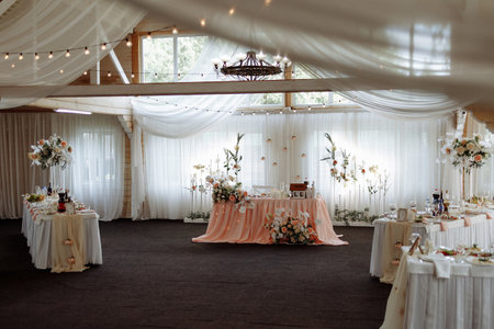 Elegant wedding banquet hall with floral decor and white drapery under wooden ceilingの写真素材