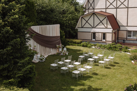 Outdoor wedding ceremony setup with white chairs and draped backdrop on green lawnの写真素材