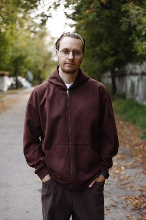 Young man in brown hoodie standing on park pathの写真素材