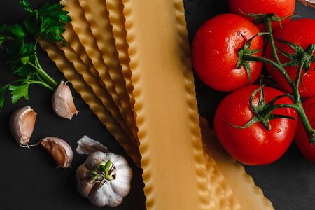 Raw lasagna ingredients and pasta products background with copy space. Top view and background of vegetables on a dark backgroundの写真素材