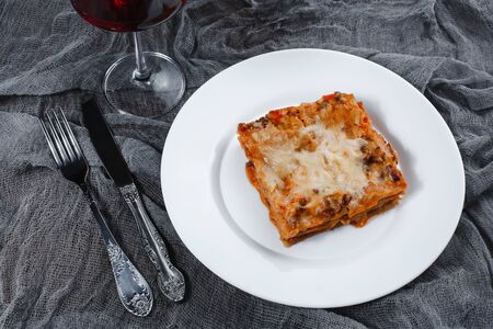 Traditional Italian lasagna with vegetables, minced meat, tomatoes and cheese on a fabric and wooden background with wineの写真素材