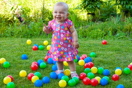 babygirl is playing with balls on green grassの写真素材