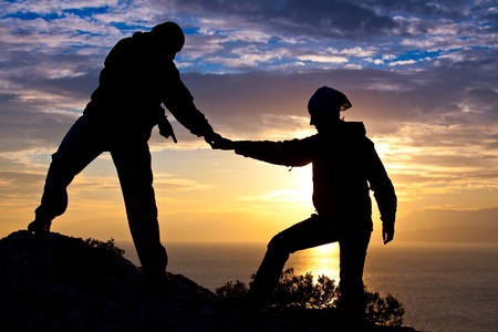 Silhouette of couple on the top of the mountain at the sea while sunsetの写真素材