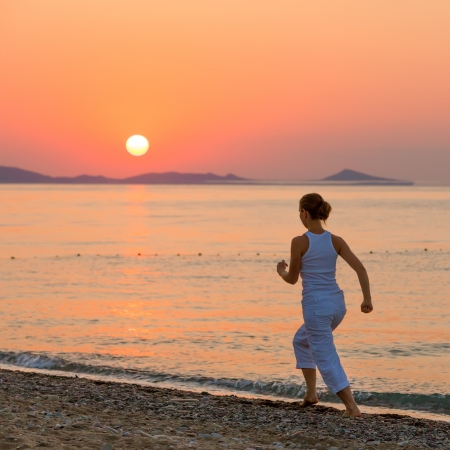 Woman is doing morning excercises at the sea during sunriseの写真素材