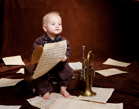 Caucasian baby boy plays with trumpet between sheets with musical notes against brown backgroundの写真素材