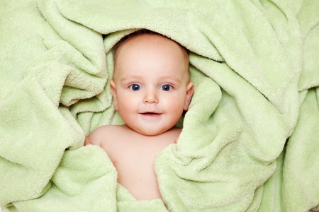 Caucasian baby boy covered with green towel joyfully smiles at cameraの写真素材