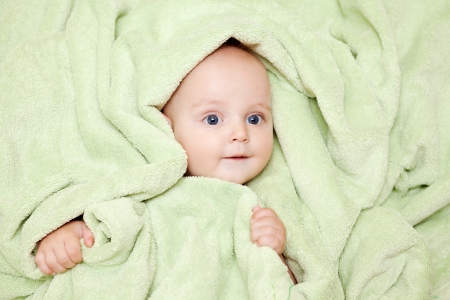 Caucasian baby boy covered with green towel joyfully smiles at cameraの写真素材