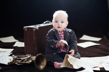 Caucasian baby boy plays with trumpet between sheets with musical notes against brown backgroundの写真素材