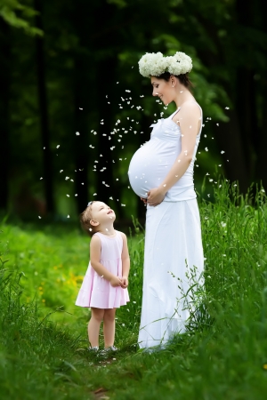 Pregnant mother and her daughter have fun outdoorの写真素材