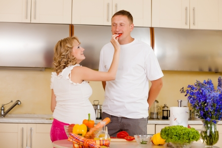 Young pregnant woman feeds her husband with vegetables at kitchenの写真素材