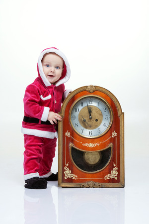 Small boy in Santa suit plays with vintage clock in white studioの写真素材