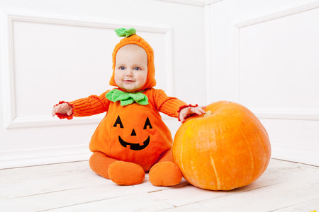 Child in pumpkin suit on white background with pumpkin の写真素材