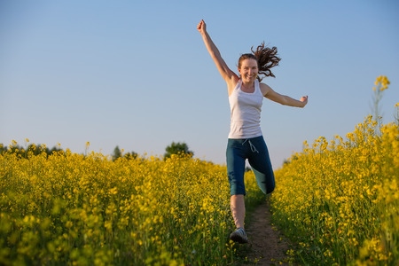 Happy woman jumps to the sky in the yellow meadow at the sunsetの写真素材