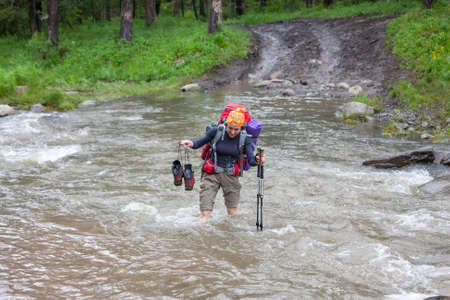 Backpackers are crossing mountain river by wooden log in Altai mountains, Russiaの写真素材