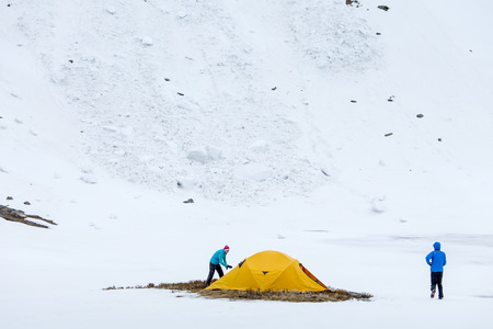Hikers set oragne tent in winter mountains on cloudy dayの写真素材