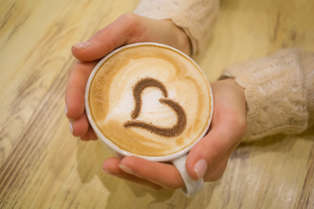woman holding hot cup of coffee, with heart shape