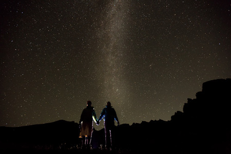 Couple is standing in mountains against night sky with milky way