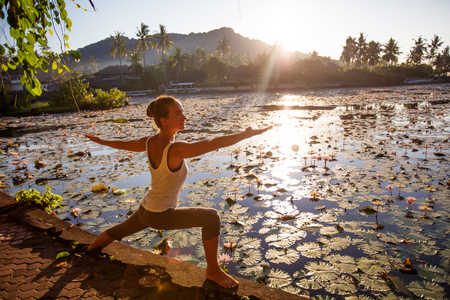 Woman practices yoga on a lake with lotus water liliesの写真素材
