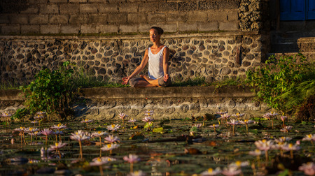 Woman practices yoga on a lake with lotus water liliesの写真素材