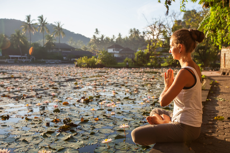 Woman practices yoga on a lake with lotus water liliesの写真素材