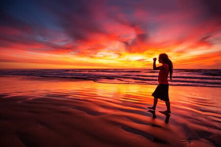 woman walking alone on the beach in the sunsetの写真素材
