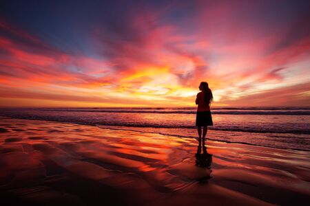 woman walking alone on the beach in the sunsetの写真素材
