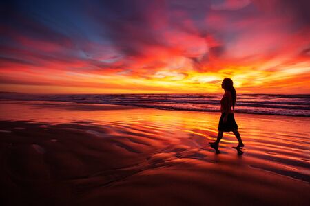 woman walking alone on the beach in the sunsetの写真素材