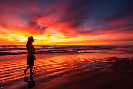 woman walking alone on the beach in the sunsetの写真素材
